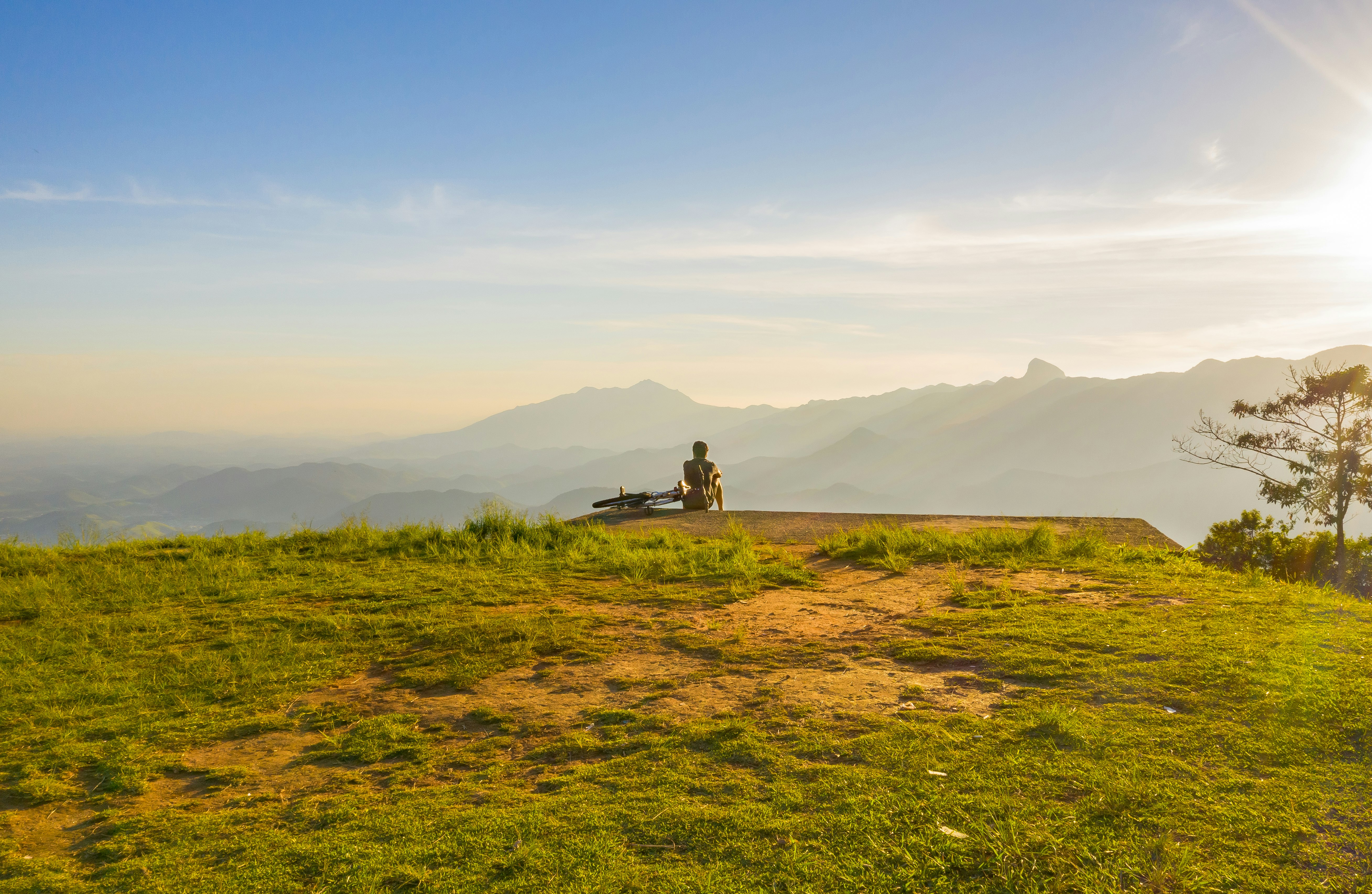 person sitting on cliff overlooking mountain during daytime